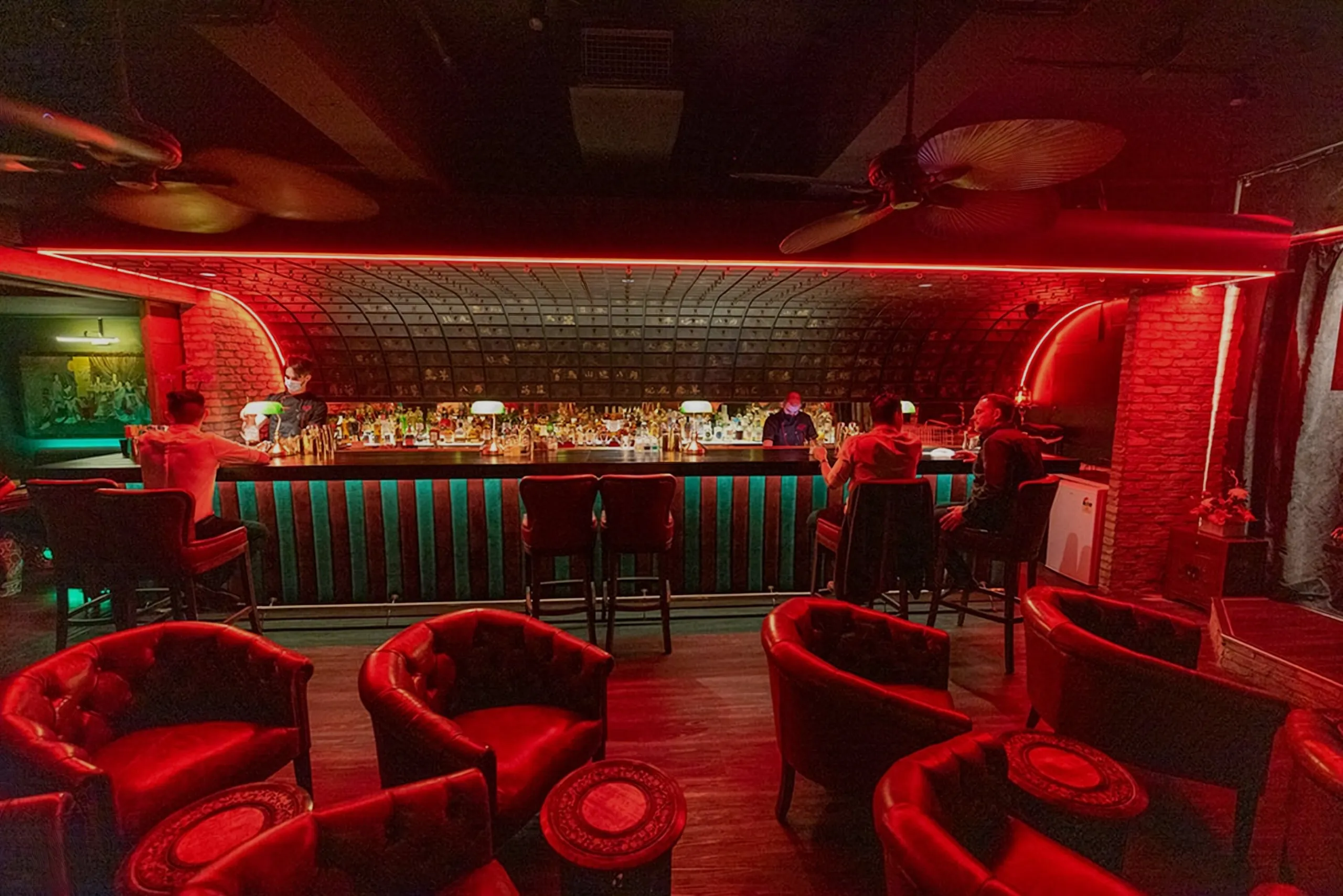 A cocktail bar lit red, with a patterned ceiling over the back bar