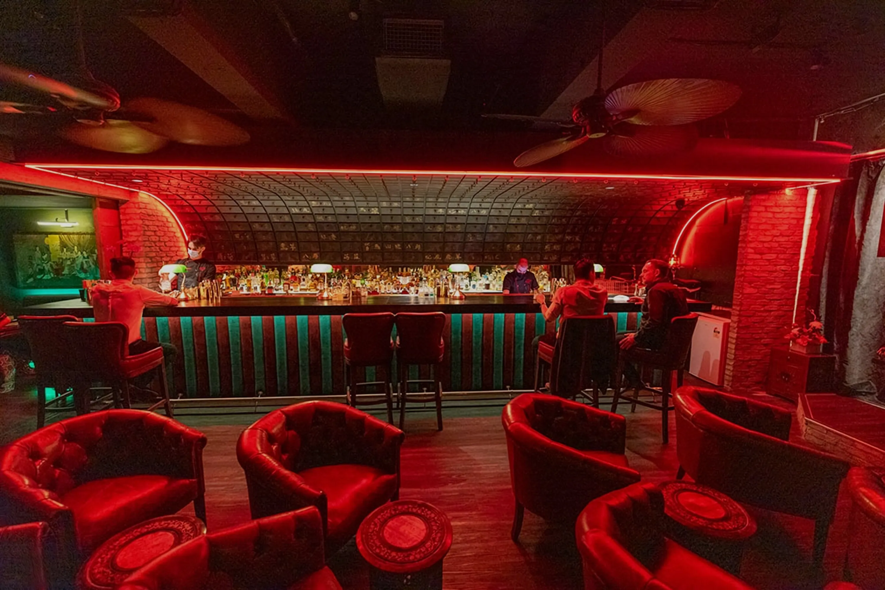 A cocktail bar lit red, with a patterned ceiling over the back bar